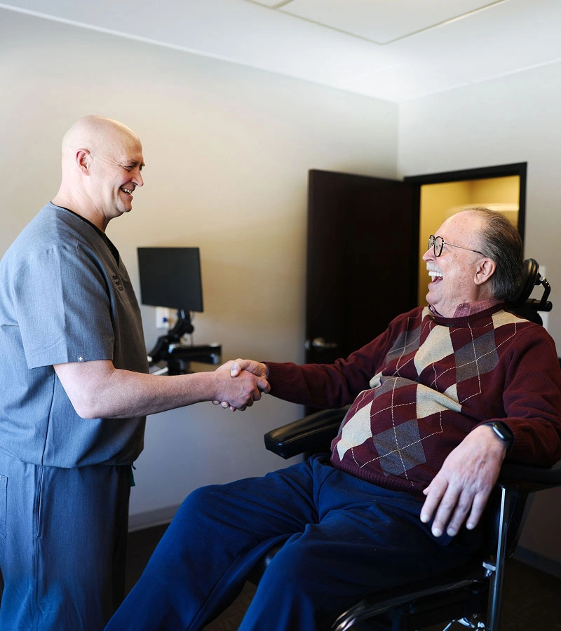 Indiana Implant Institute doctor warmly greeting a smiling elderly patient with a handshake during a dental implant consultation.