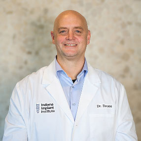 Dr. Michael Drone, Prosthodontist at Indiana Implant Institute, smiling in a white lab coat