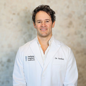 Dr. Timothy Surber, Oral & Maxillofacial Surgeon at Indiana Implant Institute, smiling in a white lab coat