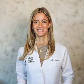 Dr. Alexandra Dann, Oral & Maxillofacial Surgeon at Indiana Implant Institute, smiling in a white lab coat