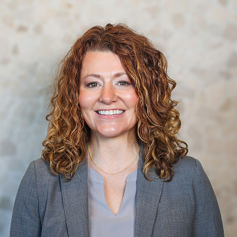 Meghan Pesich, Treatment Coordinator at Indiana Implant Institute, smiling in a grey blazer