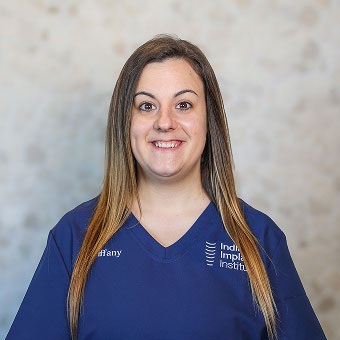 Tiffany Copollo, Prosthodontic Assistant at Indiana Implant Institute, smiling in blue scrubs